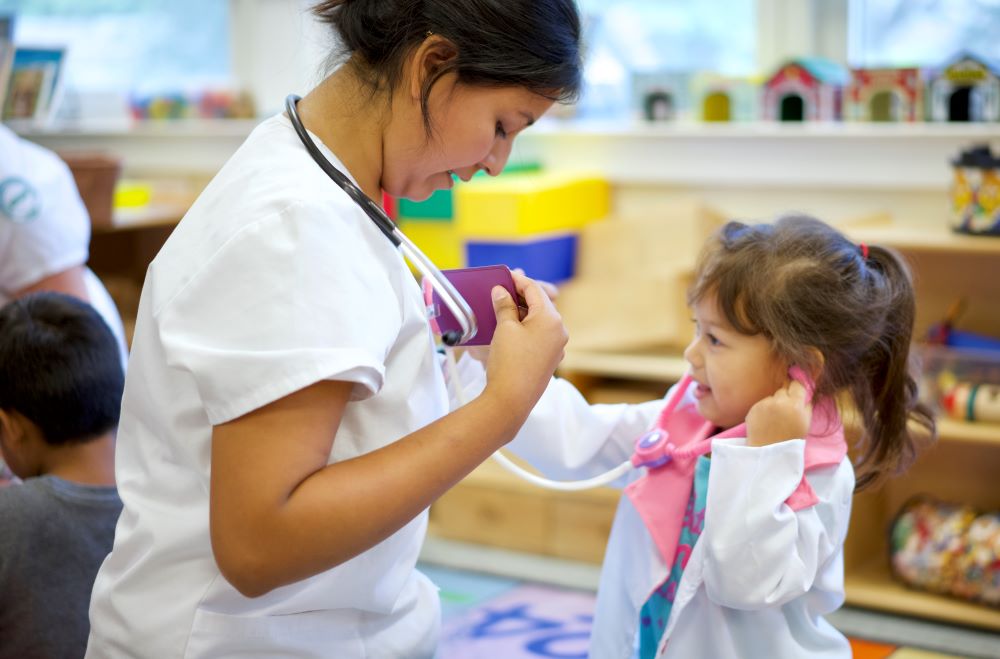 A young girl using a toy stethoscope to listen to the heartbeat of an adult.