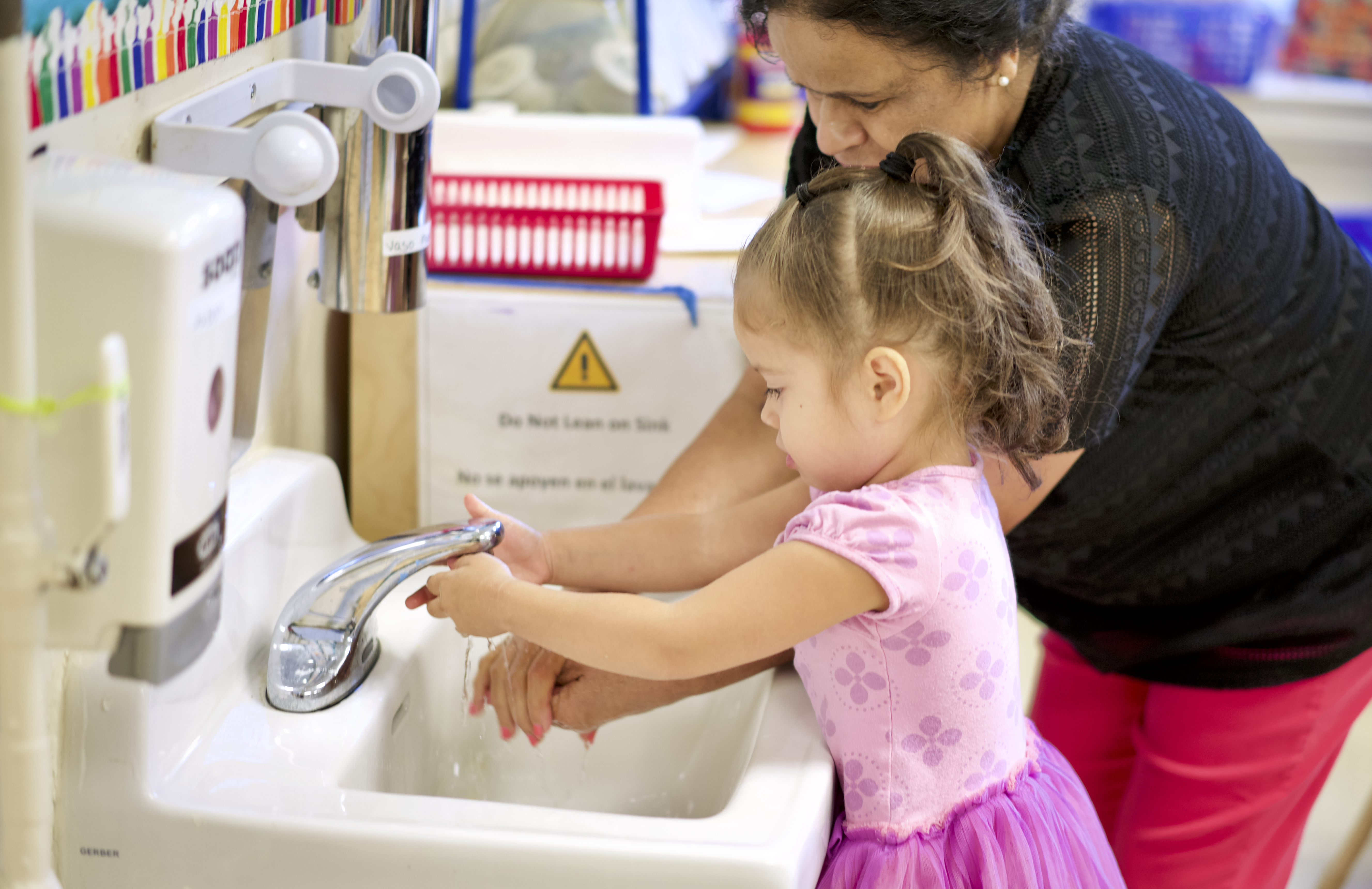 Adult helping child wash their hands at the sink.