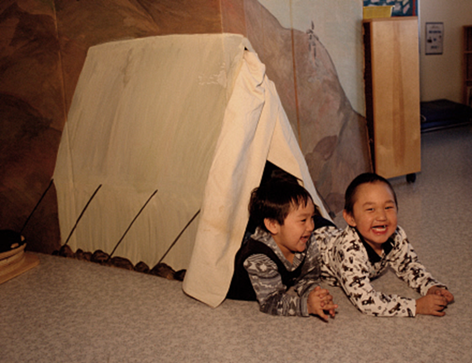 Dos niños dentro de una tienda armada con una manta.