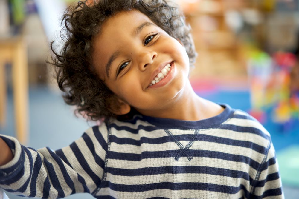 A smiling young child with their head cocked to one side.