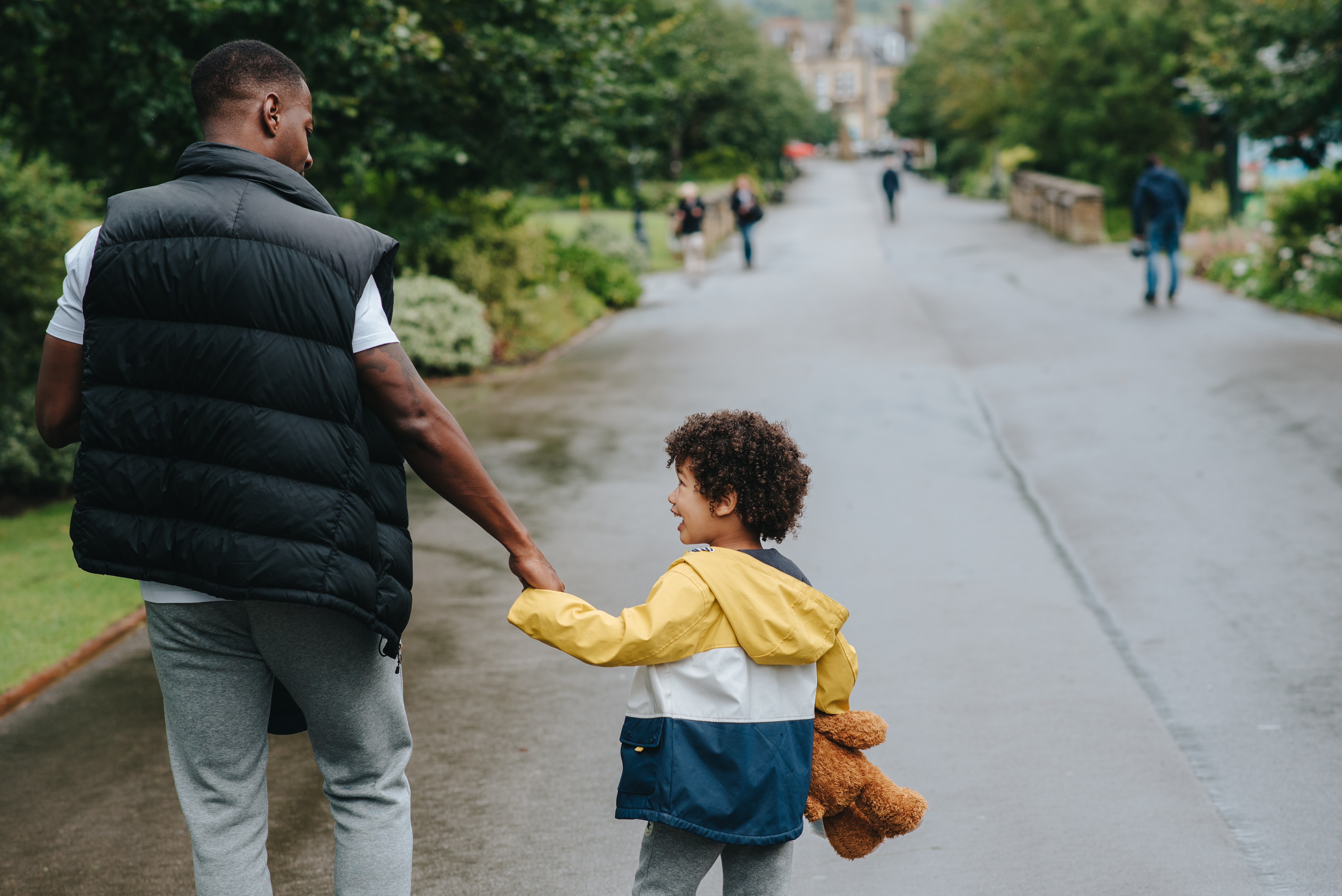 A man holding a young boy's hand as they walk in the park.