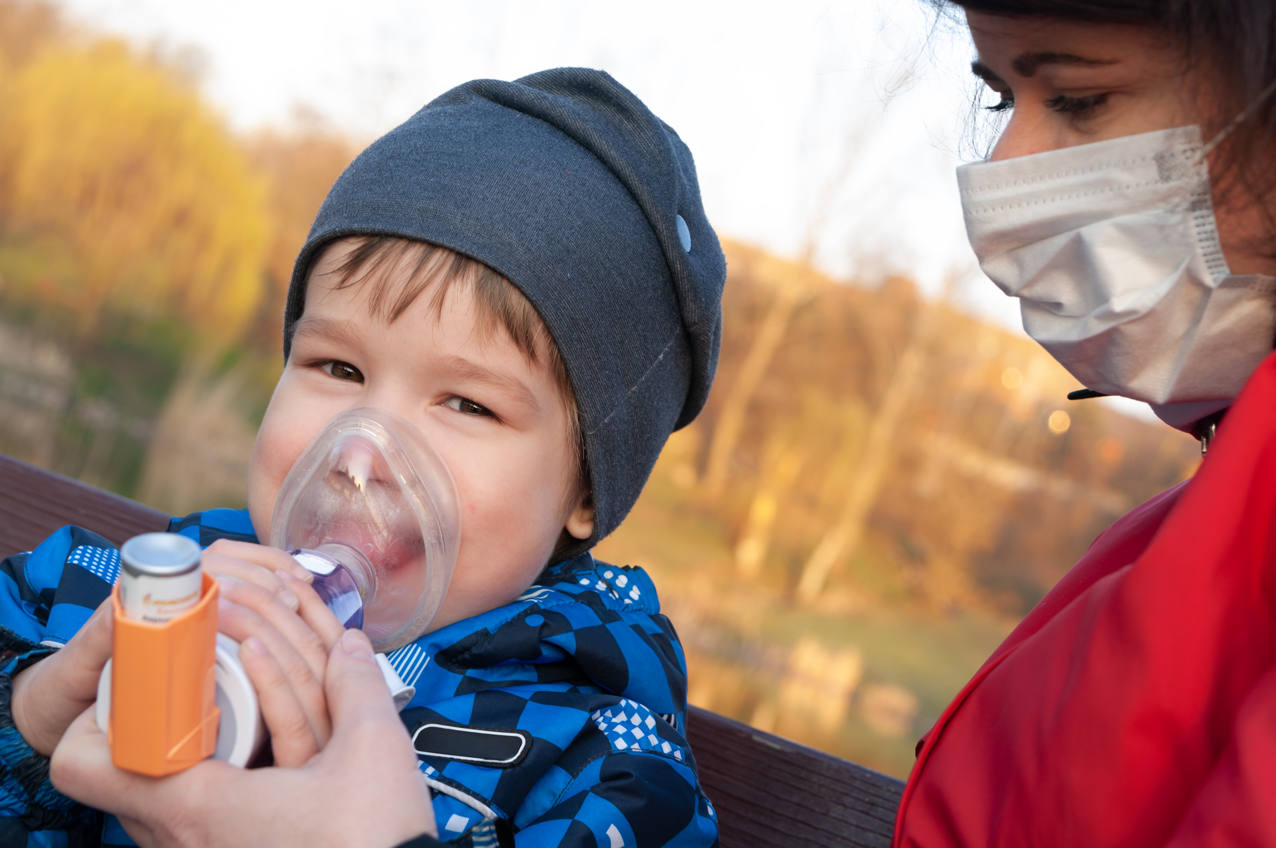 Young boy being helped by an adult to properly use his asthma inhaler.