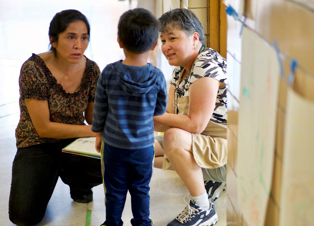 Two women kneeling down to talk with a young boy.