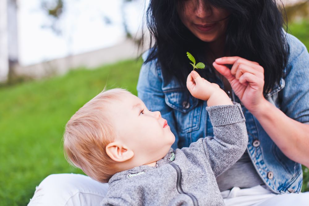 Infant and mother examing a small leaf.