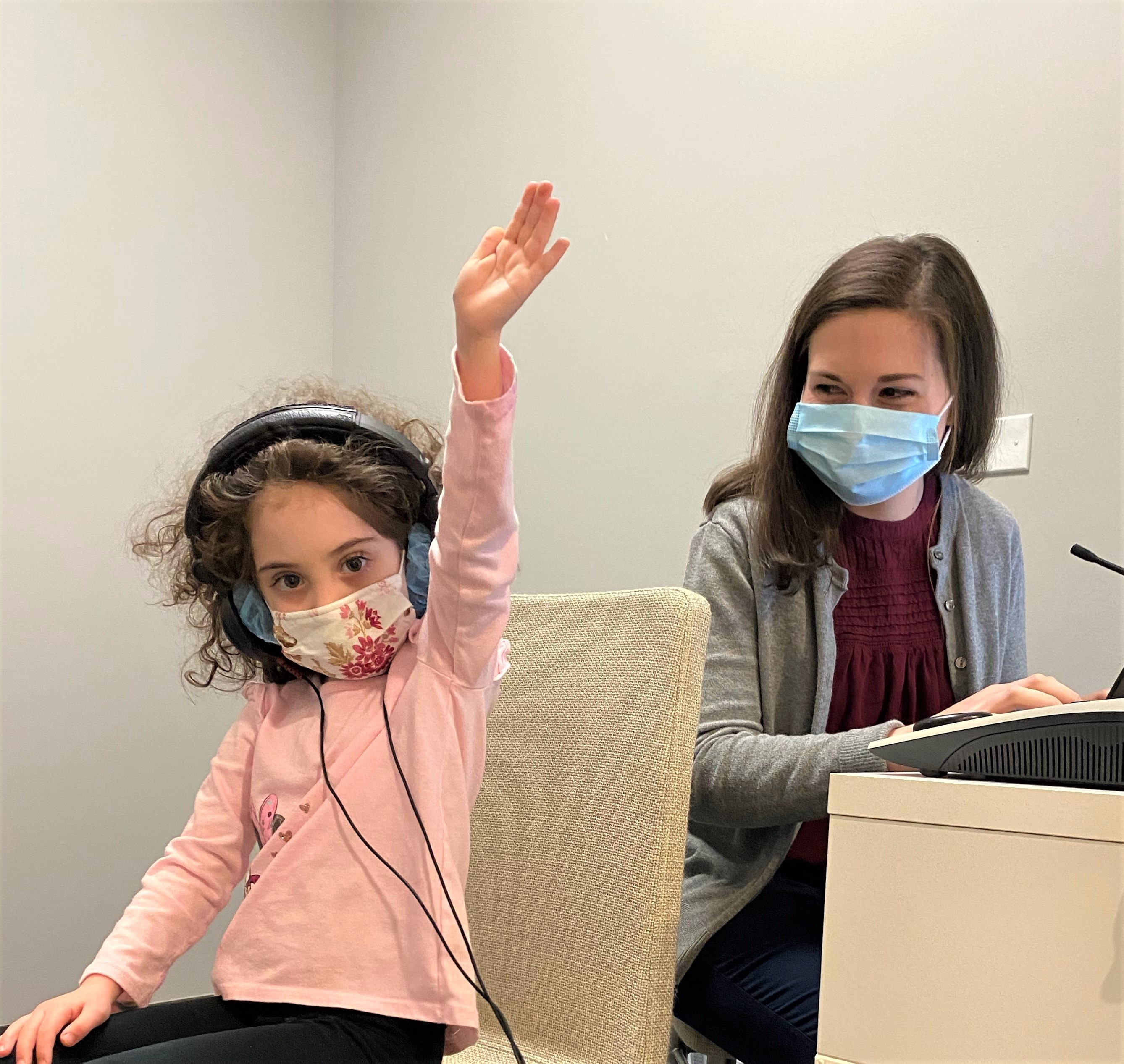 Young girl raising her hand to signify she hears a sound during a hearing screening.