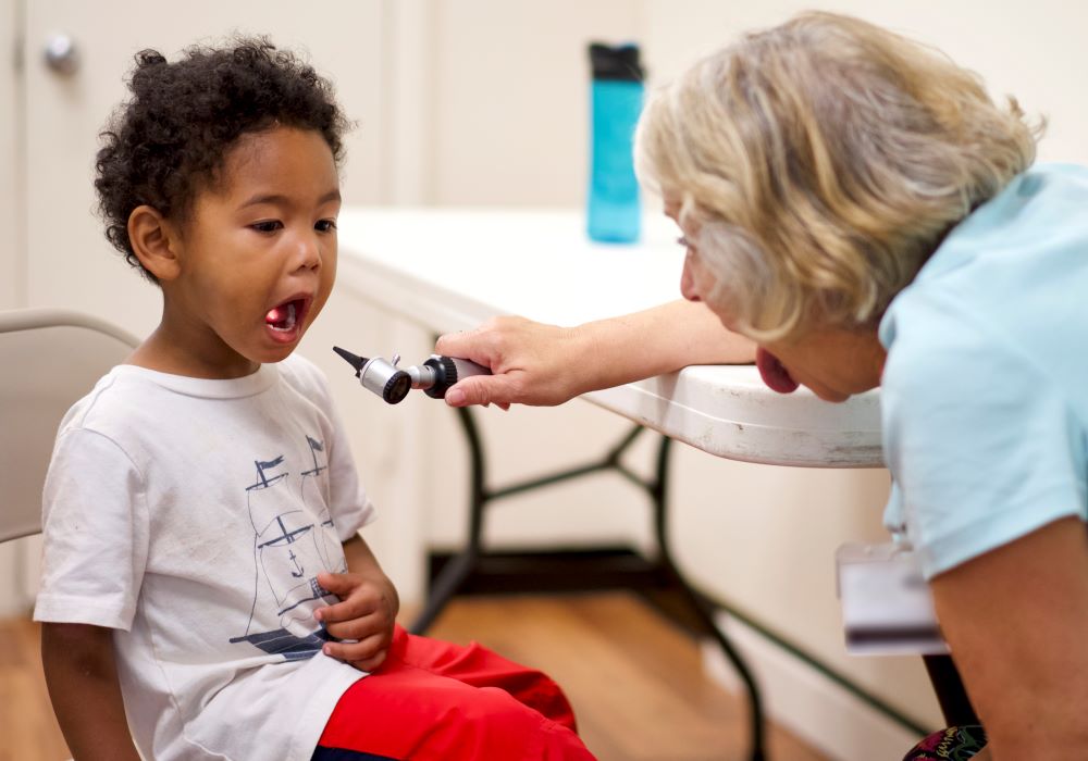 Un médico que usa una luz para mirar la boca y garganta de un niño.