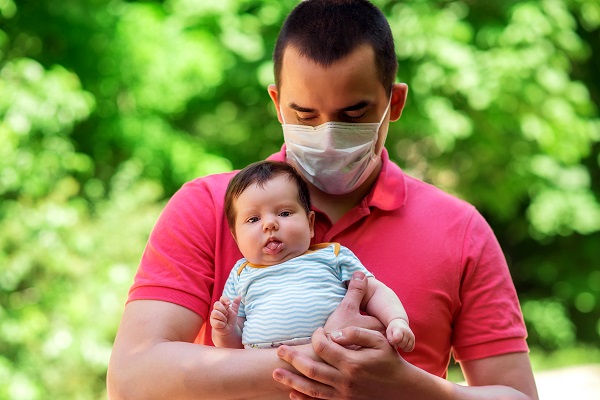 Padre con una mascarilla, sosteniendo a su bebé.