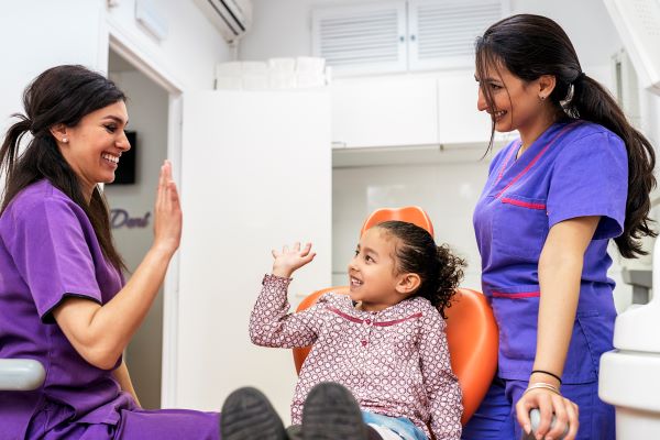 Child at dentist office high-fiving dental staff.