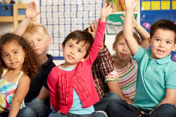 Children sitting on floor and raising their hands.