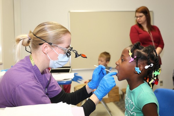 A dentail hygenist checking a young girl's teeth.