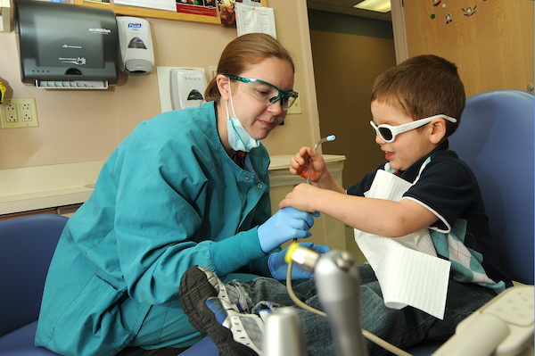 Un dentista mostrándole a un niño con gafas protectoras las herramientas que está usando.