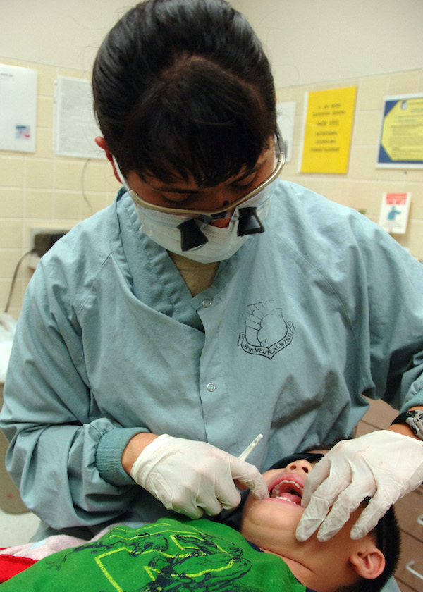 Dentista con gafas protectoras examinando la boca y los dientes de un niño.