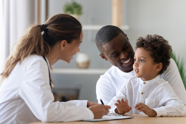 Padre e hijo sentados en una mesa hablando con una doctora.