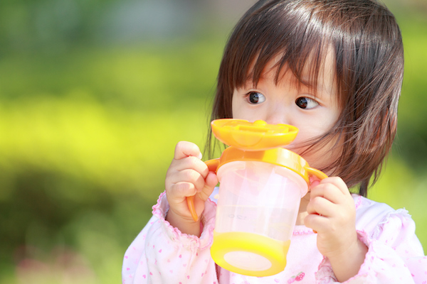 Young girl drinking water out of a large yellow sippy cup.