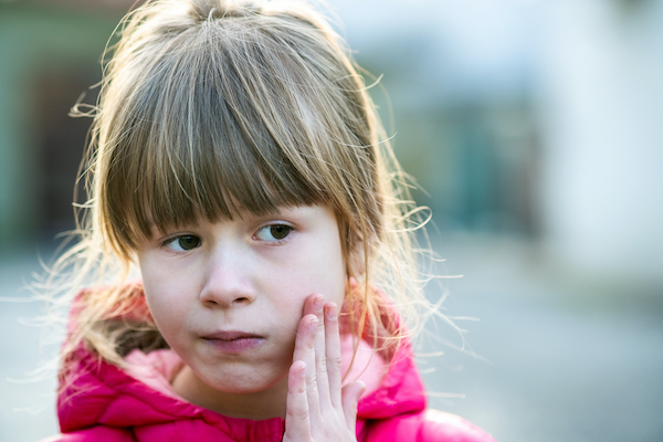 Niña con la mano en la mejilla izquierda debido a un dolor de muelas.