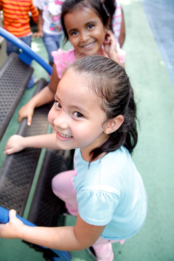 Two young girls smiling as they climb a ladder on a playground.