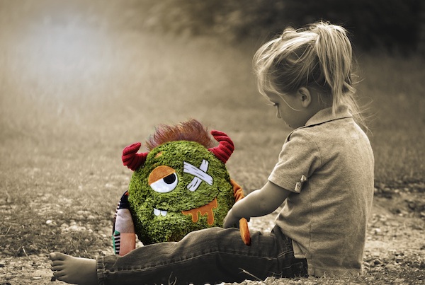 Young girl sitting on floor with a stuffed toy that has an X for one of its eyes.