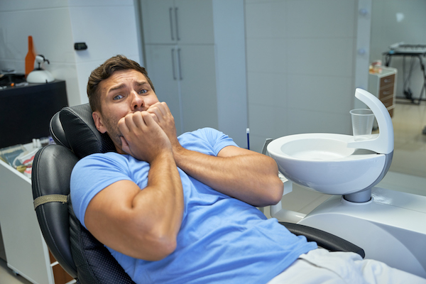 Un hombre con las manos sobre la boca porque tiene miedo de ir al dentista.