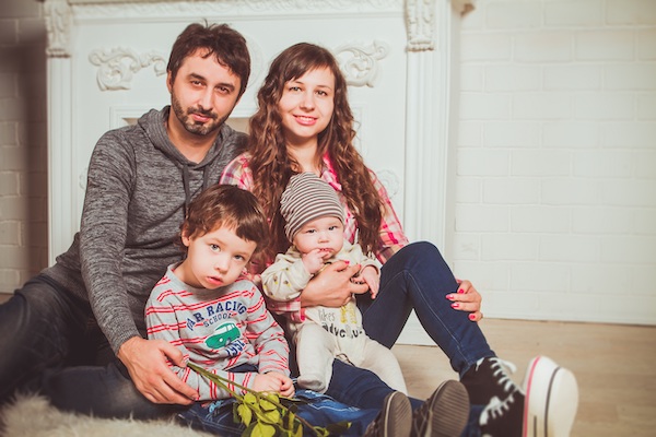 Mom and dad with their two small children sitting on the floor looking at the camera.