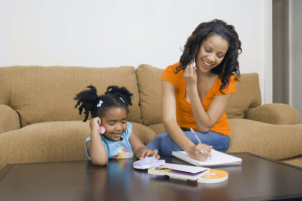 Mother and daughter writing and reading on the coffee table in front of sofa.