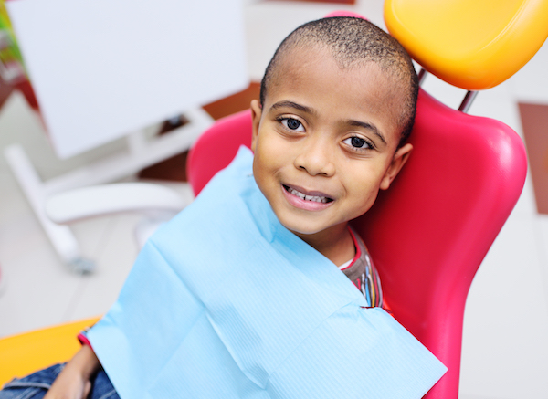 Niño sonriente sentado en una silla de dentista roja y amarilla.