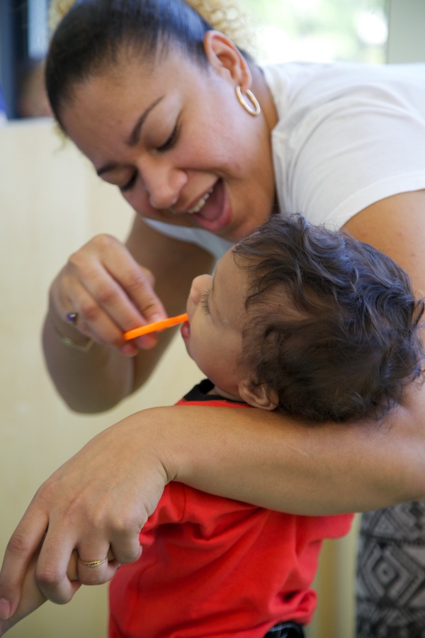 Maestra cepillando los dientes de un bebé mientras lo sostiene junto a ella.