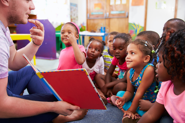 Teacher showing children a book and pointing to his mouth and teeth.