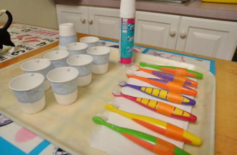 A tray with an assortment of colorful toothbrushes and small cups with mouth rinse.