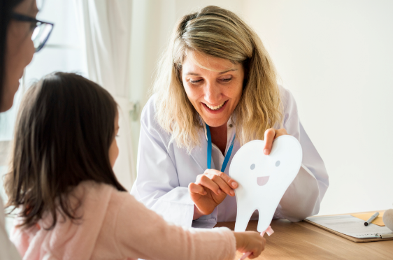 Dentist showing child a large cardboard tooth.