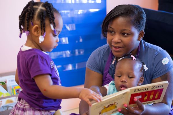 Teacher and two young girls reading a book.