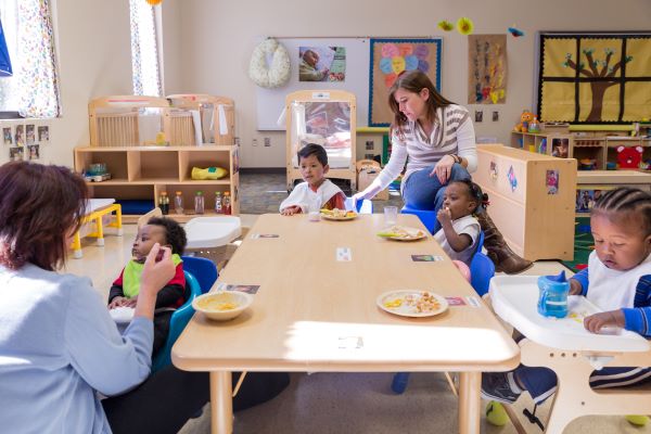 Un grupo de niños y personal reunidos alrededor de una mesa central en el salón.