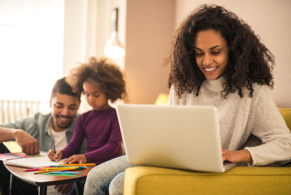 Madre usando una computadora mientras el padre ayuda al niño con la tarea.