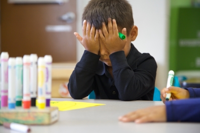 Niño en una mesa cubriéndose los ojos con las manos como si renunciara a una tarea escolar.