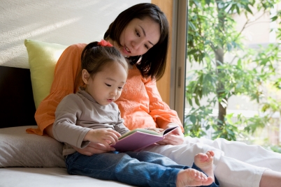 Mother and daughter sitting beside each other reading a children's book.