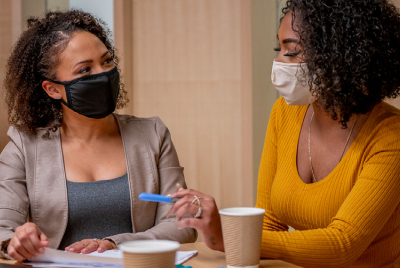 Dos mujeres con mascarillas reunidas en una mesa.