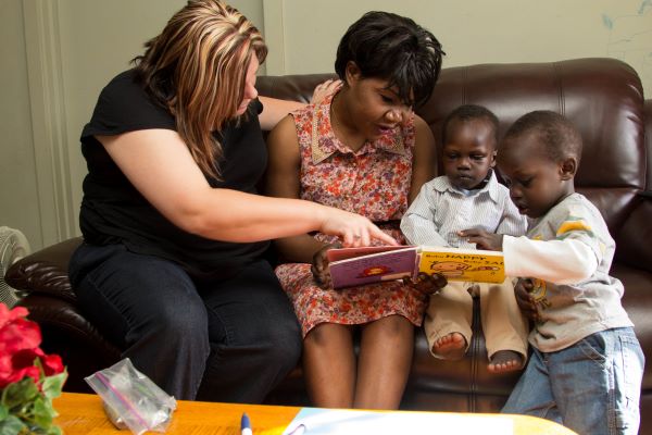 Home visitor and mother reading from a book to children.