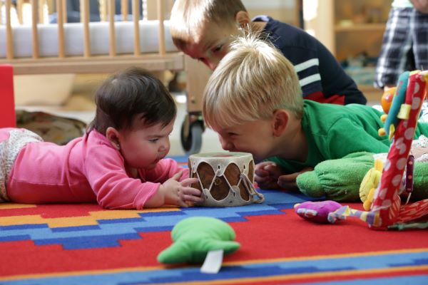 Two toddlers on their bellies handling a toy drum.