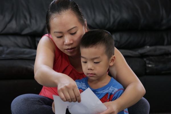 Una madre sosteniendo un papel para leer frente a su hijo.