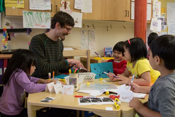 Teacher at a table engaged with children in a project.