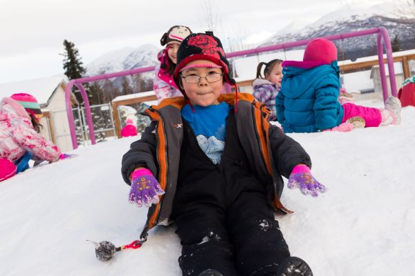 Niño sentado y deslizándose por una colina nevada.