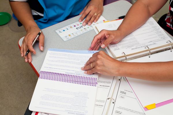 Close up the hands of two adults flipping through a binder of printed pages.