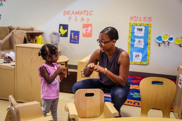 A teacher squats down to show a child something.