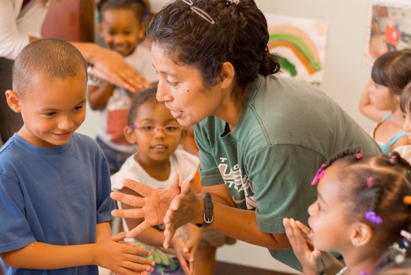 Una maestra les muestra a unos niños cómo poner las manos y luego abrirlas.