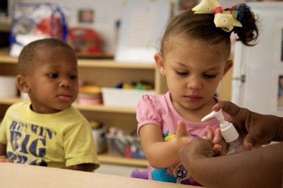 Children using hand sanntizer under adult supervision.