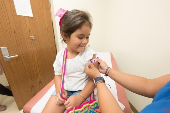 Niña con una curita colorida en el brazo izquierdo después de vacunarse.