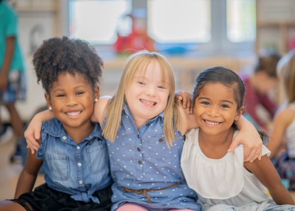 Three smiling young girls posing shoulder to shoulder.