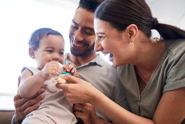 A child with a pacifier being held on the laps of his parents.