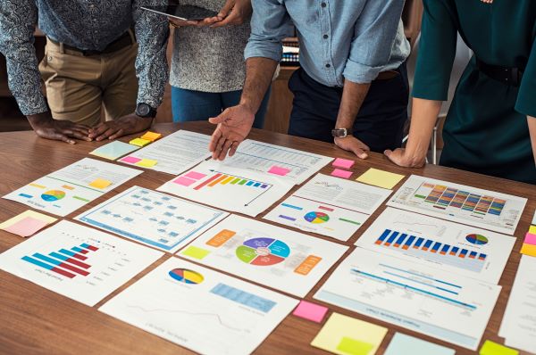 People looking over printed charts arranged on a tabletop.