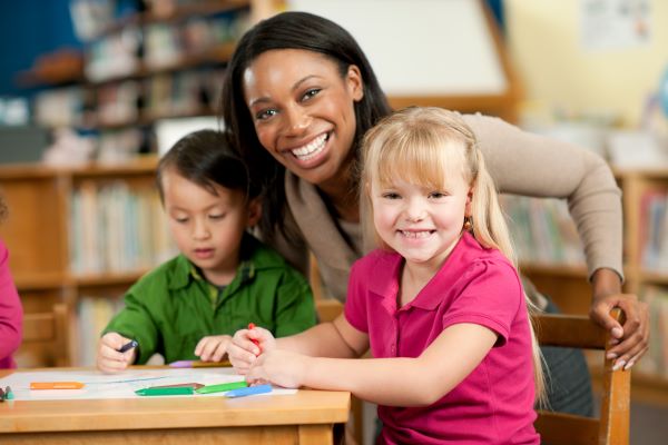 Una maestra y tres niños pequeños dibujando en una mesa.