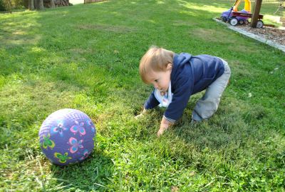 Niño encorvado hacia adelante sobre la hierba, mirando una pelota grande frente a él.